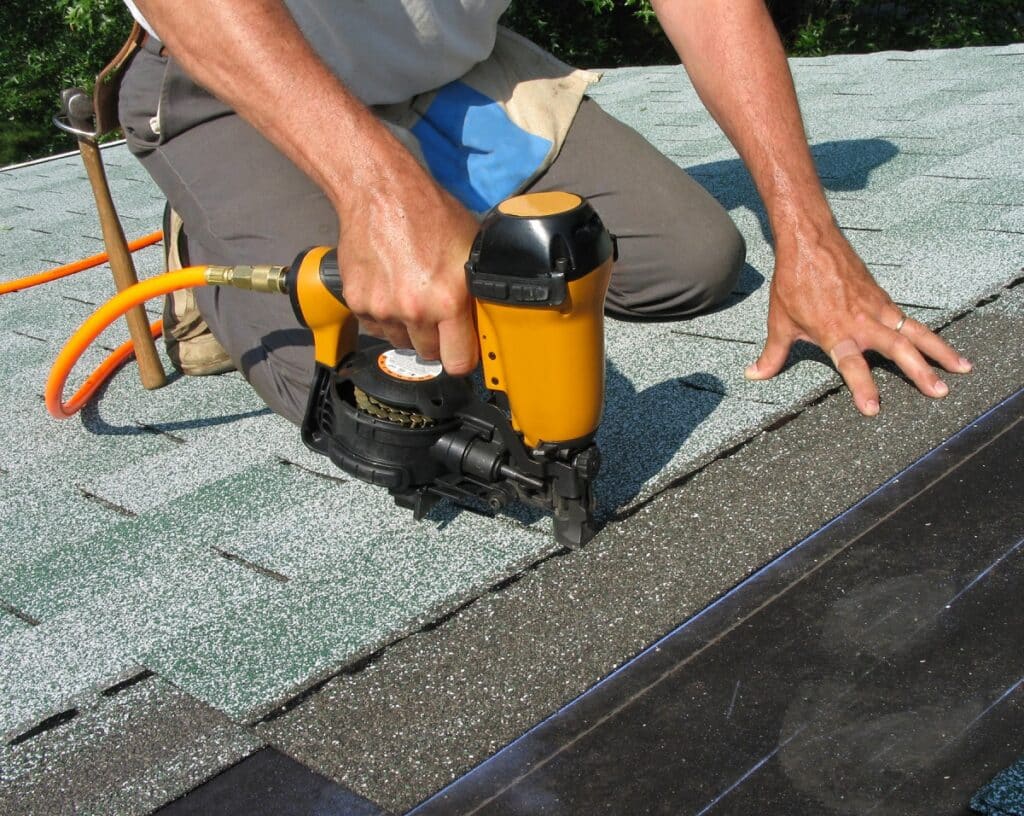 Man using nail gun to apply asphalt shingles